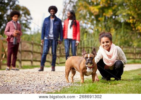 Mixed race girl squatting to pet her dog during a family walk in the countryside looking to camera, low angle
