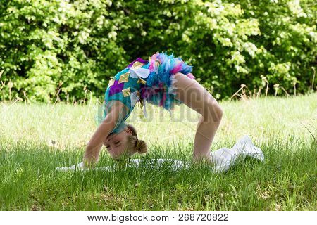 A Little Girl Doing A Yoga Backbend Wheel Pose On A Green Grass. Stretching And Fitness Training On 