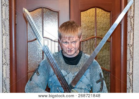 A Man Dressed Up In A Knights Hauberk At Home In His Room. Knights Sword In The Hands Of A Man. Knig