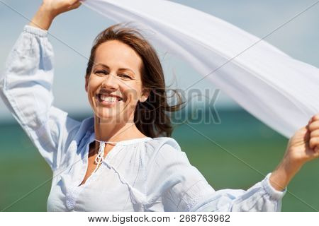 people and leisure concept - happy woman with shawl waving in wind on summer beach