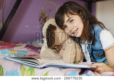 7 Years Old Girl Reading A Book On Bed