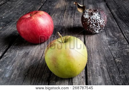 Rotten And Healthy Apple On Wooden Table.