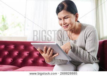 Cheerful Old Asian Woman Using Apllication On Tablet Computer