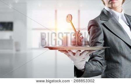 Closeup Of Waitresss Hand In White Glove Presenting Stone Key Symbol On Metal Tray With Office View 