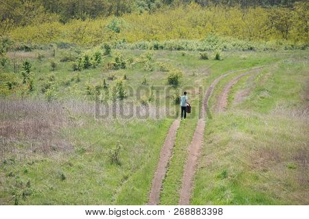 Back View Of Hipster With Suitcase In Hands Walking On Old Road In Empty Place