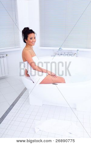 Joven hermosa mujer asiática sentada en el cuarto de baño moderno con jakuzzi