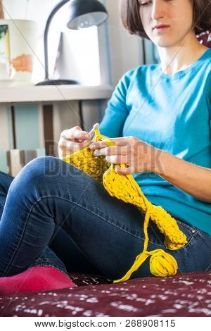 Woman Knits Crochet. The Girl Sits On The Couch And Knits From Knitting Yarn. Crochet Thick Threads.