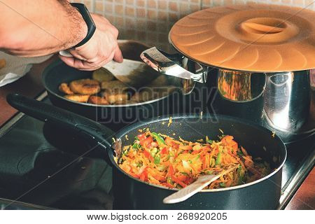 View Of The Kitchen. Pots With Cooked Food On The Stove.the Man Cooks Chicken Meat, Fried Potatoes A