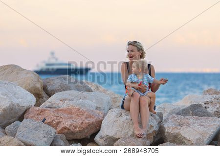 Woman Playing With Her Baby Outside Against The Sea. The Concept Of A Happy Full-fledged Family Life