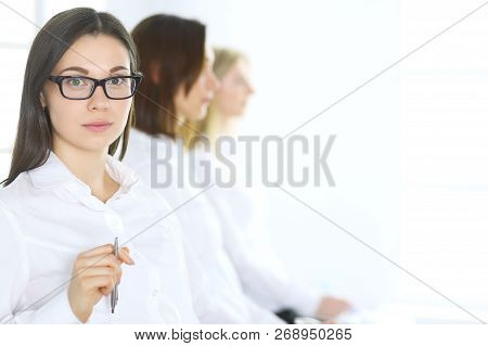 Attractive Businesswoman At Meeting Or Conference Against The Background Of Colleagues. Group Of Bus