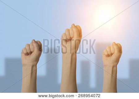 Female Hand Clenched Into A Fist And Raised Up On A Blue Background. Concept Of Power, Rebellion, Un