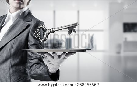 Cropped Image Of Waitresss Hand In White Glove Presenting Big Key On Metal Tray With Office View On 