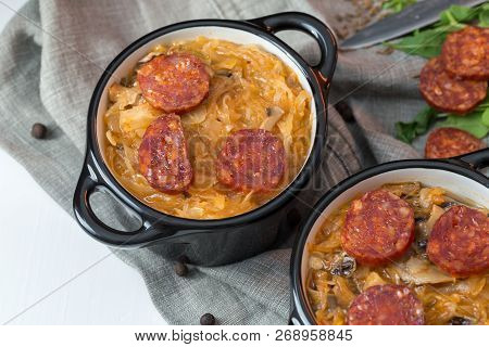 Slovak Christmas National Cabbage Soup In Two Small Black Pots With Sausage On The Tablecloth Backgr