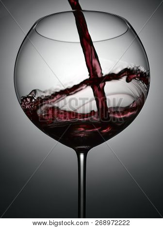 Red Wine Splashing Into Glass On Gray Background With Glow