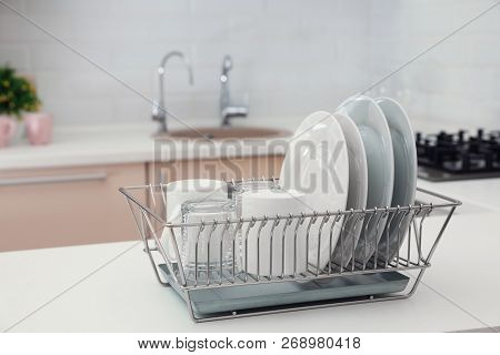 Dish Drainer With Clean Dinnerware On Table In Kitchen