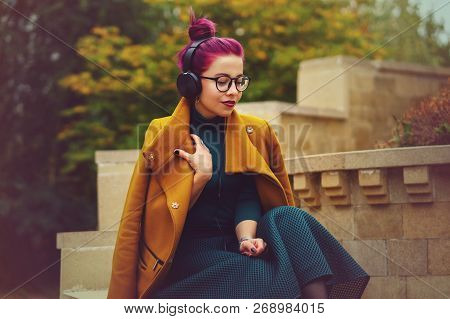 Cute Young Girl Listening To Music On Headphones In Autumn Park. Girl Has Eggplant Hair. Woman Enjoy