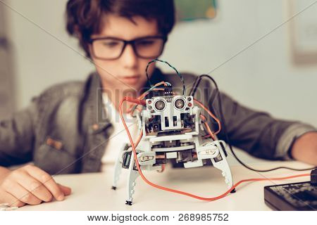 Boy Sitting At Desk And Constructing Robot At Home. Young Boy In Shirt. Indoor Joy. Modern Hobby Con