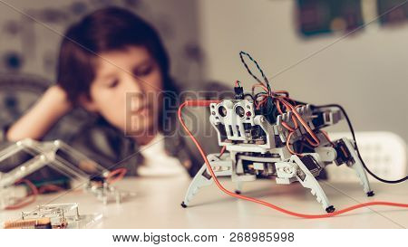 Boy Sitting At Desk And Constructing Robot At Home. Young Boy In Shirt. Indoor Joy. Modern Hobby Con