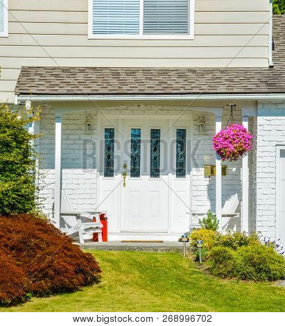 Entrance Of Residential House Decorated With Backet Of Flowers, Two White Chairs And Red Churn