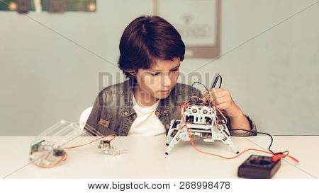 Boy Sitting At Desk And Constructing Robot At Home. Young Boy In Shirt. Indoor Joy. Modern Hobby Con