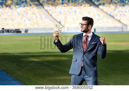 Smiling Young Businessman In Suit And Glasses With Money Showing Yeas Gesture At Stadium