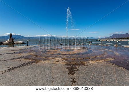 Fountain Spraying The Ground With A Jet Of Water On The Promenade Of Lake Chapala, The Pier And The 