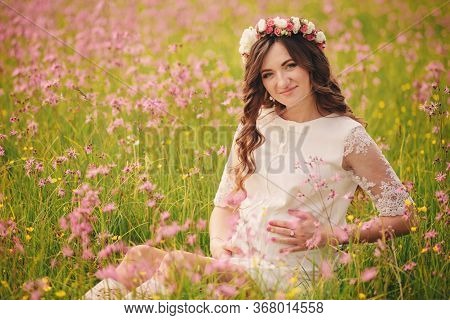 Portrait Of A Pregnant Woman Sitting In Fieid Of Pink Flowers. Young Beautiful Pregnant Girl With A 