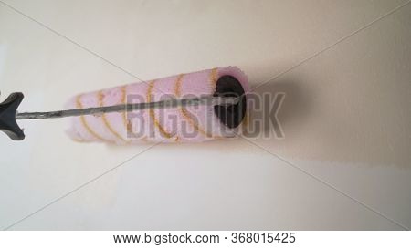 Background Of Paint Roller Standing Against Blank White Wall. Lubricates The Wall With A Primer. A W