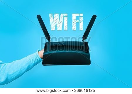Black Wifi Router On Hand And Wifi Inscription Over Blue Background