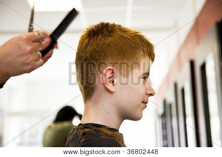 Smilende ung dreng med rødt hår hos frisøren