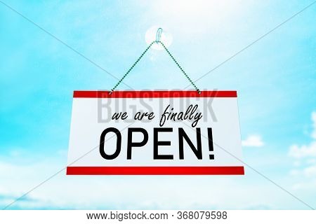 COVID-19 WE'RE FINALLY OPEN ! sign hanging on window store end of confinement stores reopening . Retail businesses opening again for non essential services. Sunny summer background.