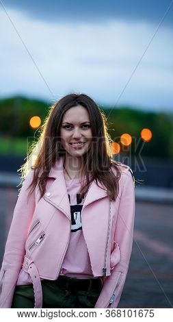 Portrait Of Pretty Smiling Girl In Pink Jacket And Blouse In Evenig In Park