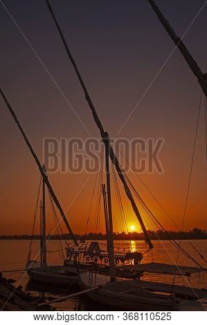 Traditional Egyptian Felluca River Boats Moored On The Nile River Bank With Sunset And Reflection In