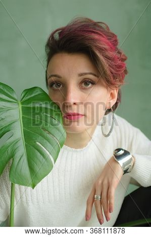 Portrait Of A Young Beautiful Woman With Perfect Smooth Skin With A Large Green Tropical Leaf. Fashi