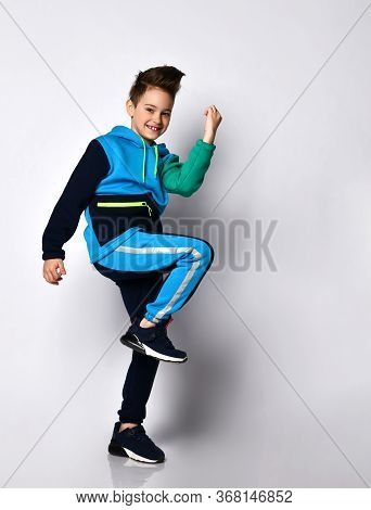 Little Brunet Model In Colorful Sport Suit, Black Sneakers. He Performing Exercises, Smiling, Posing