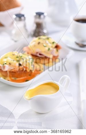 Hollandaise Butter Sauce In A Gravy Boat For Breakfast Served With Eggs Benedict- Fried English Bun,