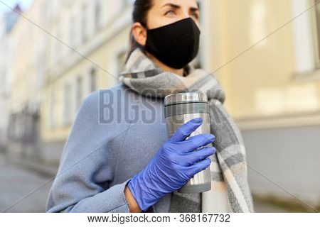 health, safety and pandemic concept - close up of young woman wearing black face protective reusable barrier mask with tumbler or thermo cup on city street