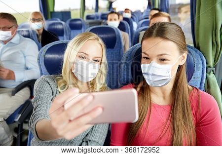 tourism, pandemic and health care concept - young women or friends wearing face protective medical mask for protection from virus disease in travel bus taking selfie by smartphone