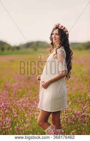 Pregnant Happy Girl Stand And Hold Hands On Stomach, Stand On Grass In The Outdoor In The Field Of P