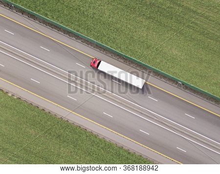 Dump Trucks Carrying Goods On The Highway. Red Truck Driving On Asphalt Road Along The Green Fields.