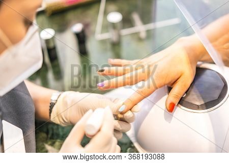 With Security Measures And Face Mask Painting Colored Nails Of The Client. Reopening After The Corod