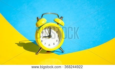 Yellow Vintage Alarm Clock On A Blue And Yellow Background With Selective Focus, Copy Space For Text