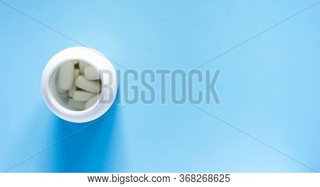 Pills Of Vitamin In The Opened White Plastic Container On Soft Blue Background.