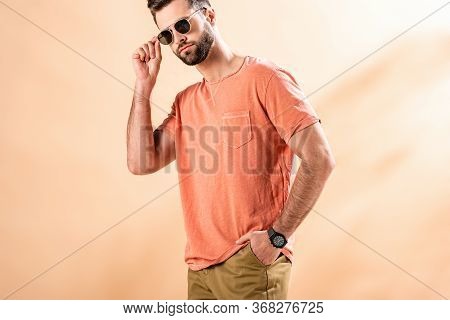 Stylish Young Man Posing In Shorts, Summer T-shirt And Sunglasses On Beige