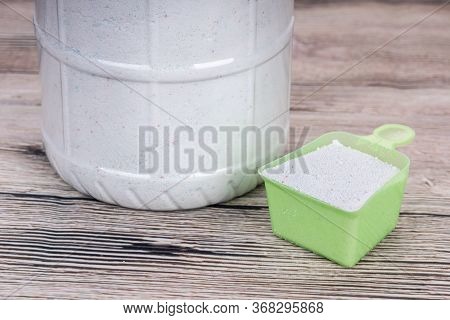 Close-up Of Laundry Detergent Powder With Scooper On Wooden Surface