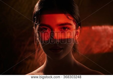 Portrait of a beautiful girl with shiny make-up and red arrows on her eyes in red light. Make-up and cosmetics concept. Beauty, fashion.