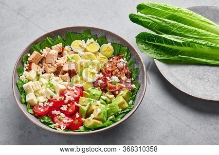 Cobb Salad In Gray Matte Bowl On Concrete Backdrop. American Cuisine Dish With Tomatoes, Chicken, Ba
