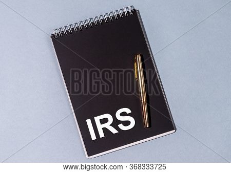 Irs Acronym Text Written On A Black Notebook Or Planner With Golden Pen On Blue Table. Tax Reminder.