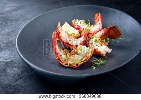 Traditional barbecue spiny lobster tail sliced and offered with lemon slice and herbs as closeup on a modern design plate 