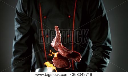 Closeup of chef throwing raw beef steaks from wok pan in fire. Fresh asian food preparation on dark background.